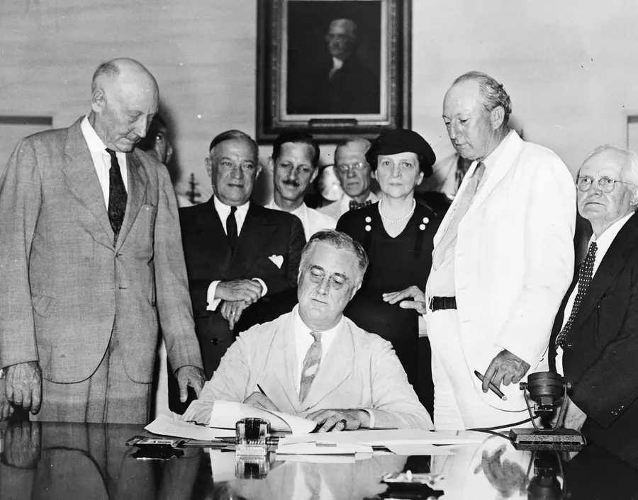 President Roosevelt signs the Social Security Act in the White House on 14 August 1935, with Frances Perkins standing behind him
