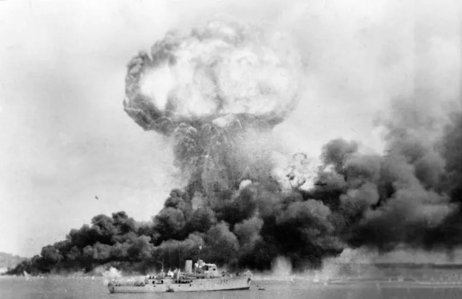 The ammunition ship MV Neptuna explodes in Darwin harbour during the first raid, 19 February 1942, with oil tanks burning behind; HMAS Deloraine is in the foreground.