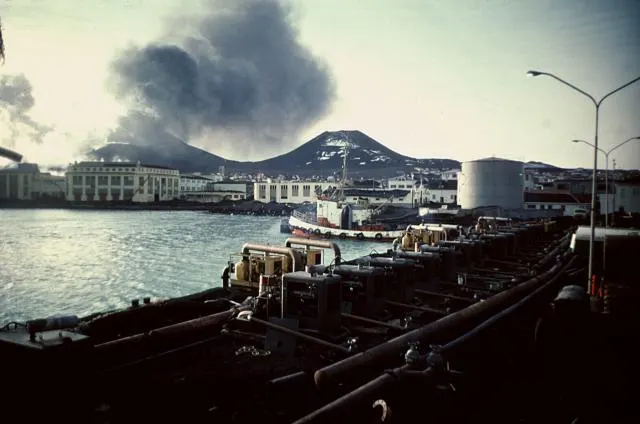 Ash rises from the new volcano behind the town of Vestmannaeyjar in 1973; in front, the pumps that sprayed sea water on the lava.