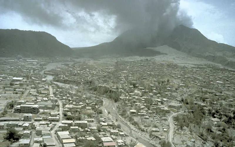 Ash-covered Plymouth, the abandoned capital of Montserrat, below the steaming Soufrière Hills volcano in July 1997