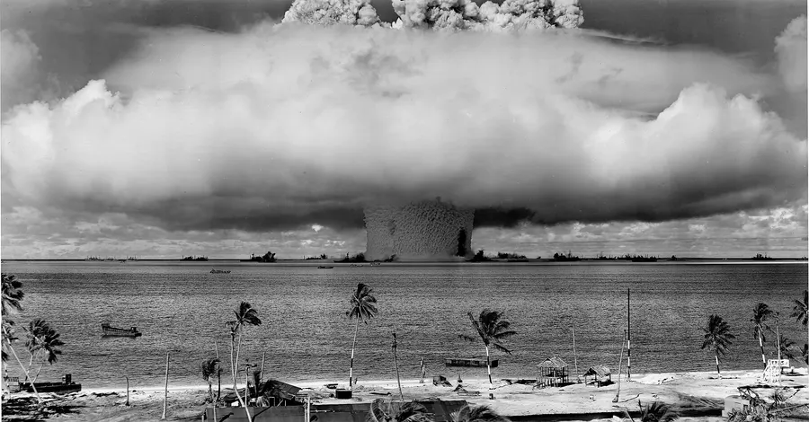 The column of water thrown up by the Baker test in Bikini lagoon, with target ships dwarfed at its foot