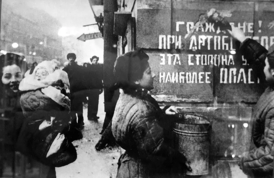 Leningraders in 1944 beside a wartime sign warning that this side of the street is the most dangerous during shelling.