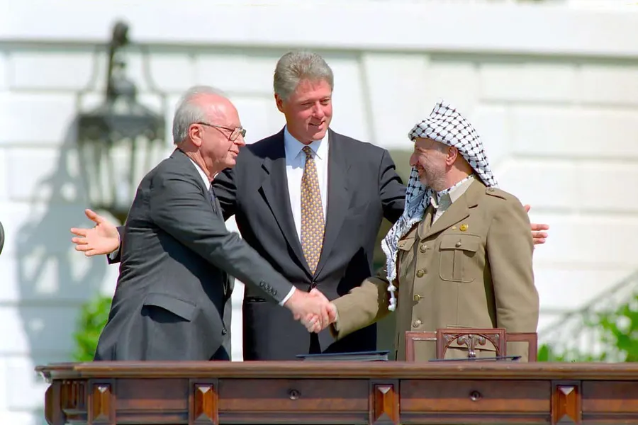 Yitzhak Rabin and Yasser Arafat shake hands, with Bill Clinton between them, on the White House lawn on 13 September 1993