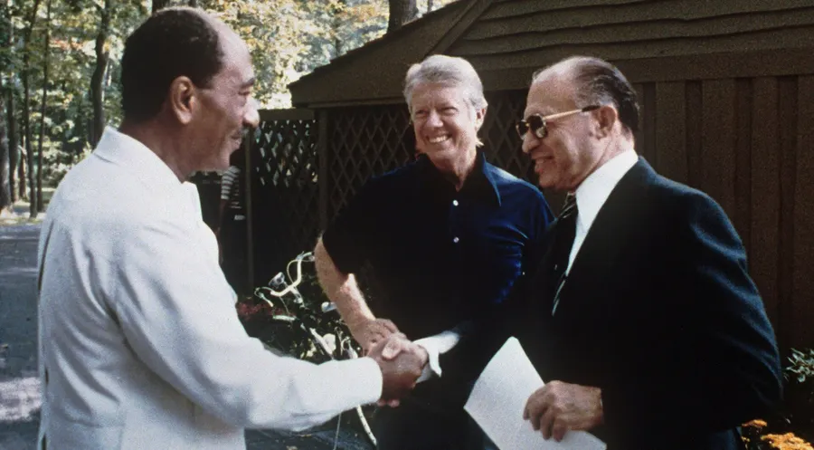 Anwar Sadat and Menachem Begin shake hands, with Jimmy Carter between them, at Camp David in September 1978
